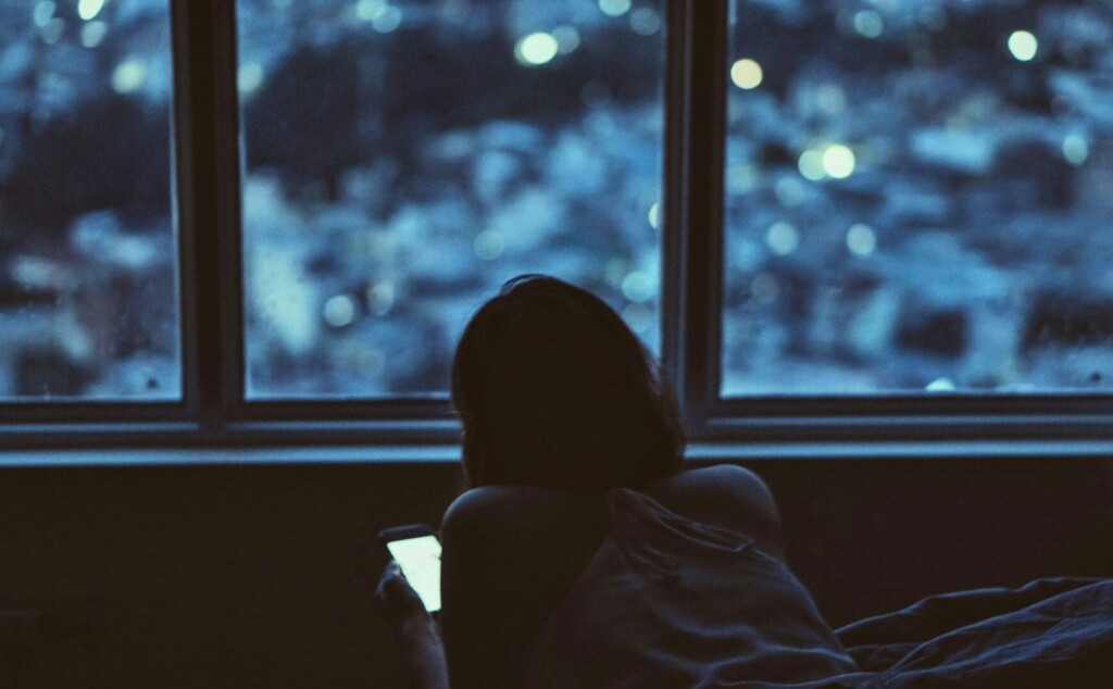 夜に窓際でスマホを見ている女性